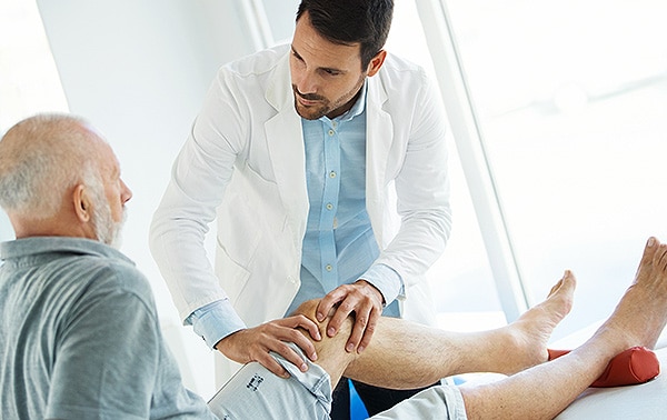 Senior man having his arthritic knee examined by a doctor
