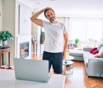 Middle age man with beard training and stretching doing exercise at home looking at sport video on computer