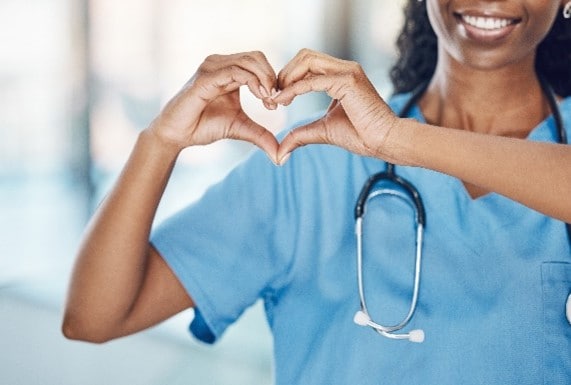 African American woman nurse making a heart shape with her hands while smiling and standing in a hospital.